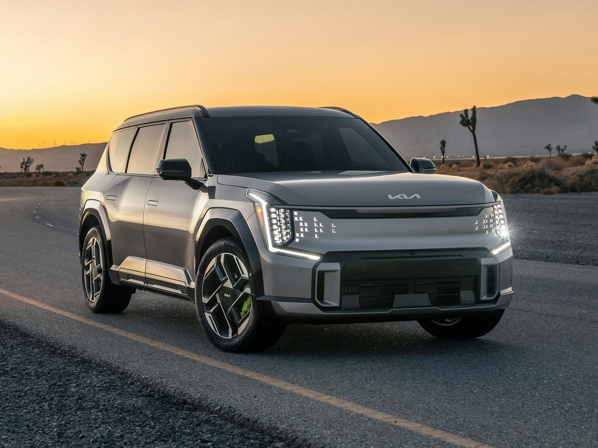 A silver three-row family SUV on a desert road at sunset